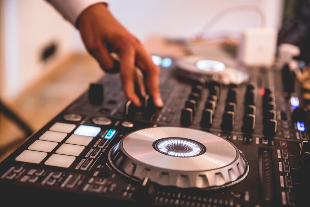 The hand of a wedding DJ rests on a knob of a turntable.