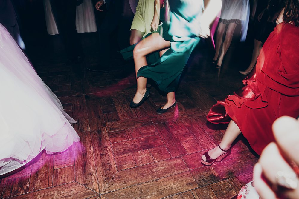 Female dress hems and feet are seen dancing on the dancefloor of a wedding.