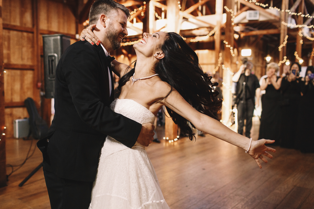 Bride shakes her dark hair while dancing with the groom at a wooden interior wedding.