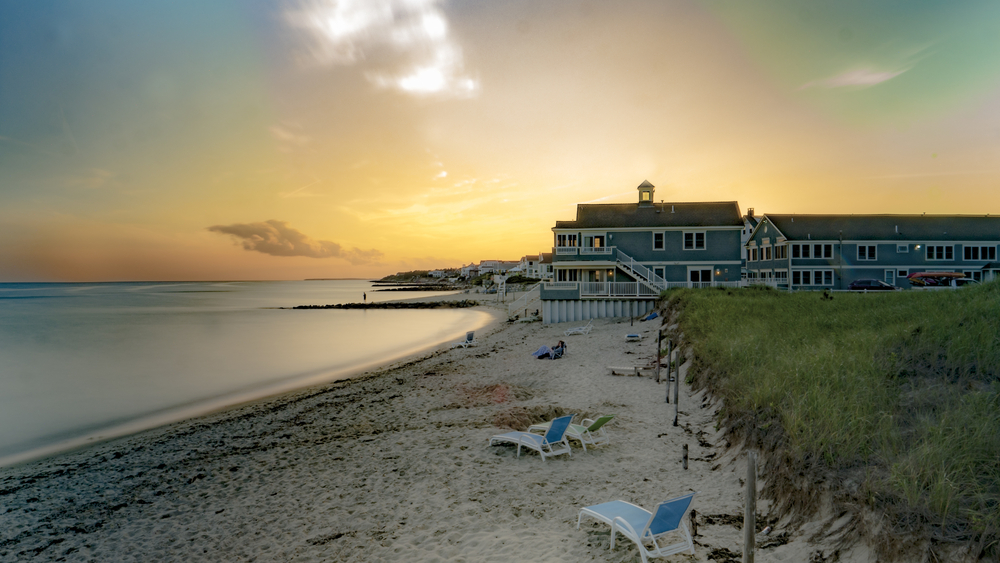 Sun sets over a beach on Cape Cod, with hotels on water in the distance.