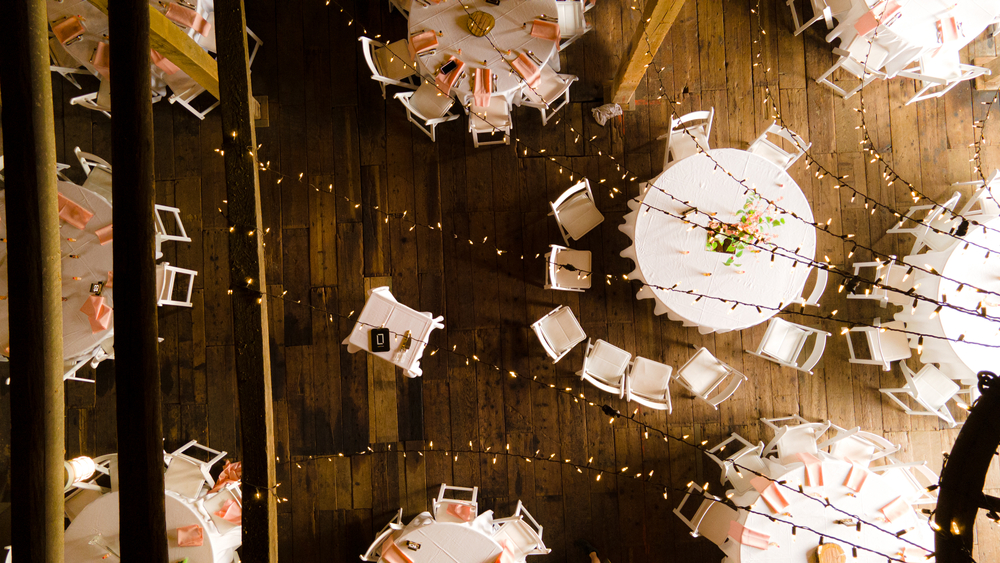 Aerial view of a barn wedding, with white tables and string lights.